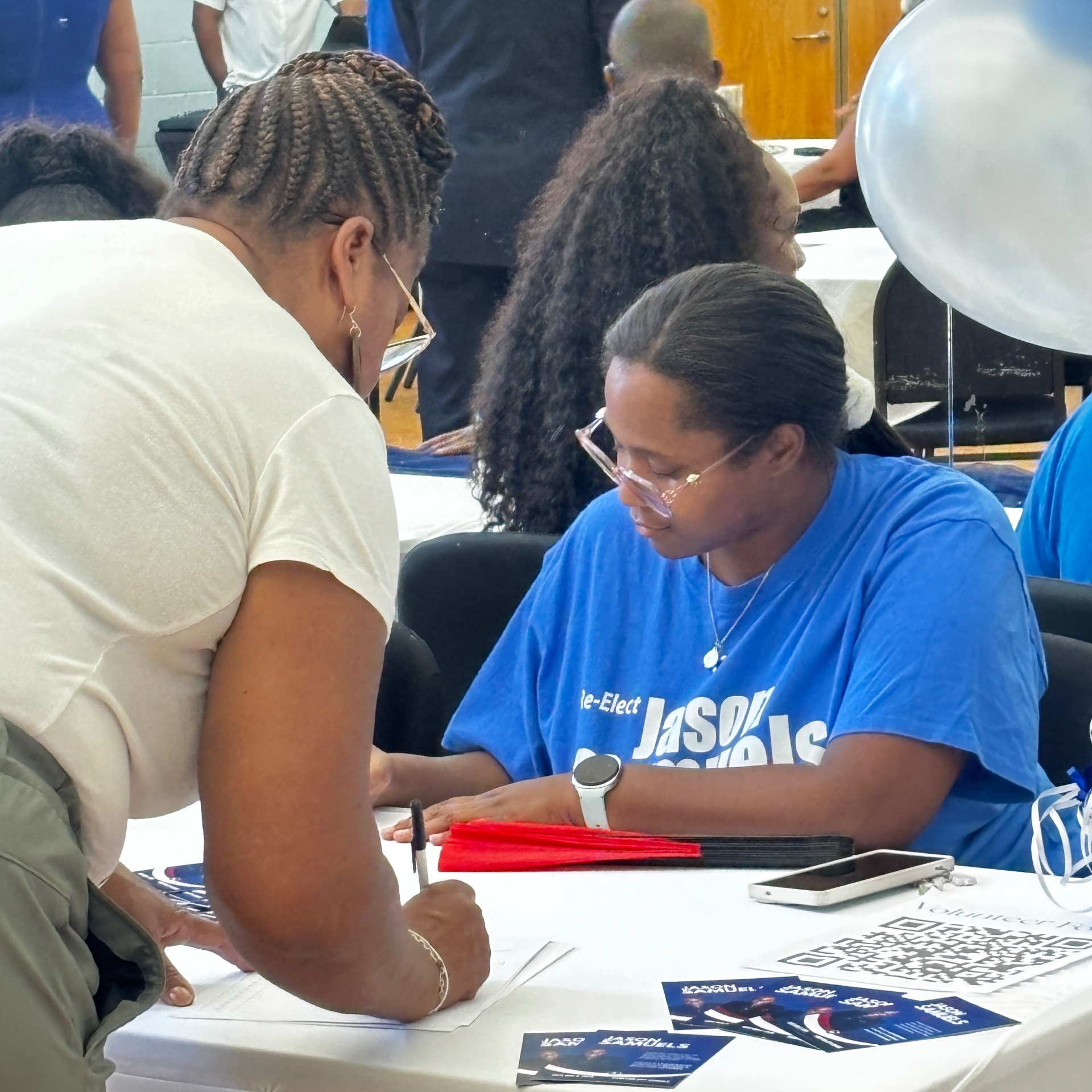 A guest signs in at the registration table while a volunteer in a Re-Elect Jason Samuels shirt looks on at the kickoff event.